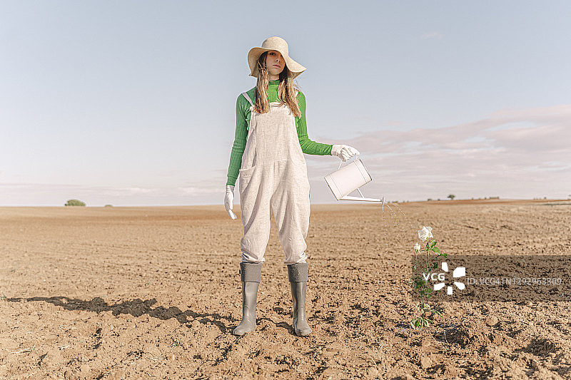 站在贫瘠田野中浇花的女人图片素材