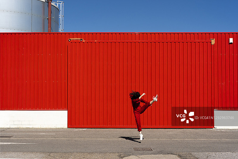 身穿红色工装裤的女人在红色卷帘门前跳跃图片素材
