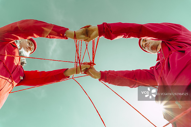 年轻夫妇身着红色衣服，用红绳在天空下表演的局部视图图片素材