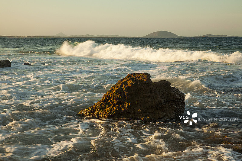 澳大利亚昆士兰州阳光海岸穆卢拉巴，傍晚光线下海浪拍打岩石架，玻璃屋山脉隐约可见图片素材