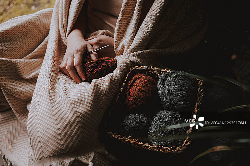 一名女子穿着米色格子呢拿着一团线和针织针，旁边是一个线篮，照片中只能看到手图片素材