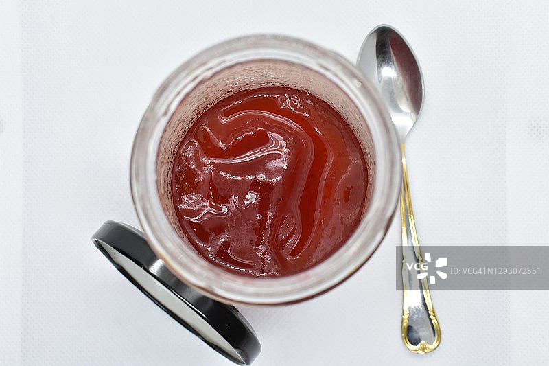 打开的罐子，里面有新鲜的草莓果酱，一个金属勺子和一个白色背景上的盖子的俯视图。水平照片。图片素材