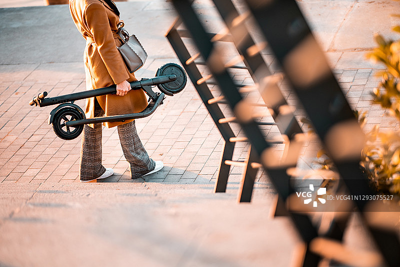 下班后，女人手拿折叠电动滑板车回家图片素材