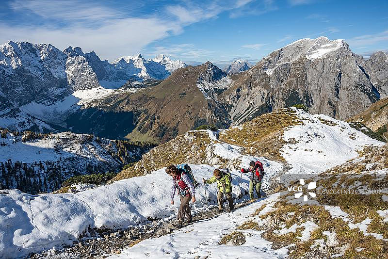 三名徒步者在秋季徒步小径上，背景是奥地利蒂罗尔卡文德尔山脉的雪山图片素材