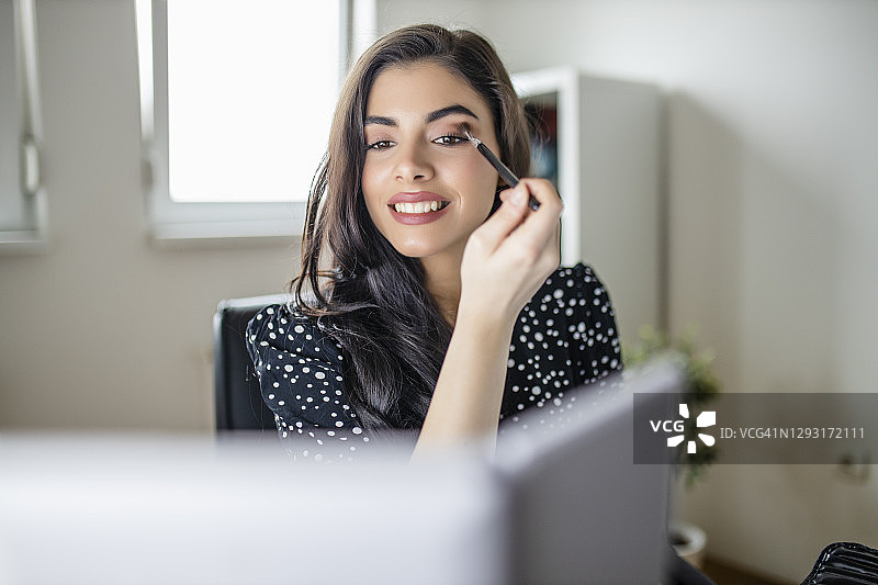 年轻女子在家庭办公室的镜子前化妆图片素材