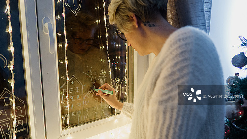 女人在玻璃窗上绘制圣诞装饰图片素材