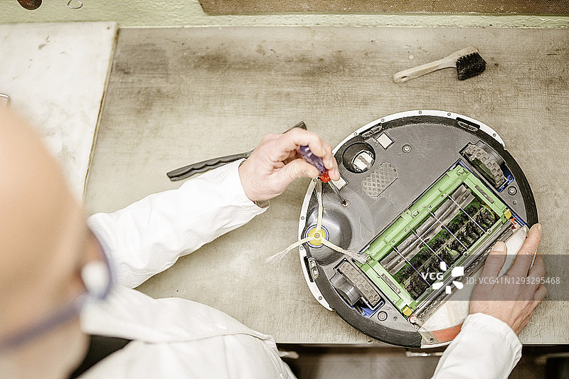 在简陋工作室修理扫地机器人的匿名男人图片素材