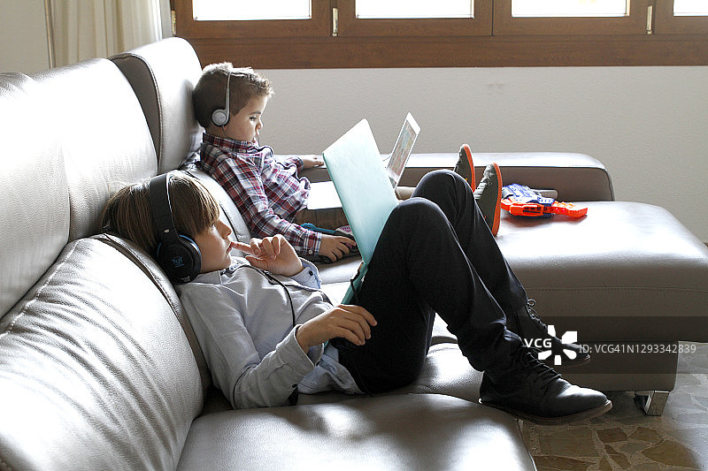 兄弟姐妹躺在沙发上使用笔记本电脑图片素材