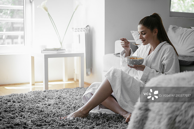 年轻女人在家中穿着浴袍吃麦片粥图片素材