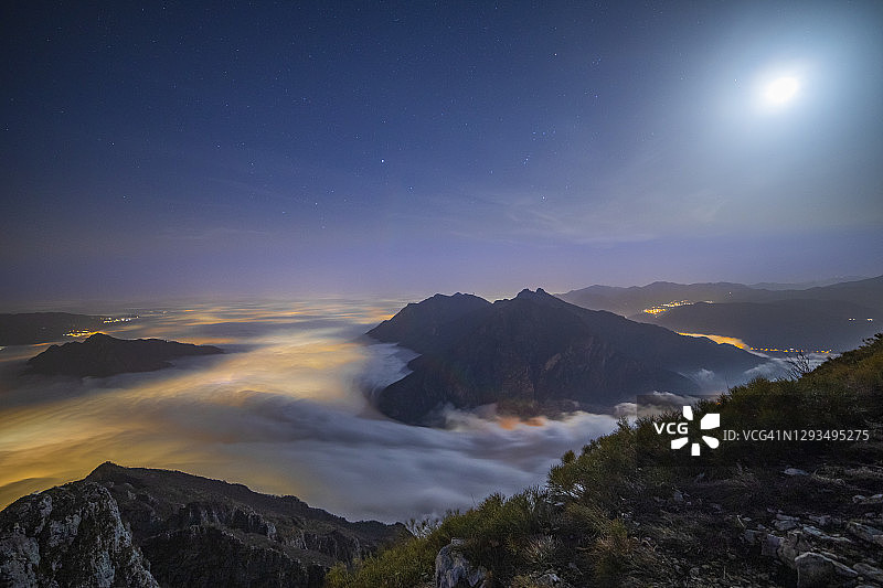 从意大利伦巴第大区莱科省科尔蒂尼奥内山顶观看莱科市灯光照亮的雾库图片素材