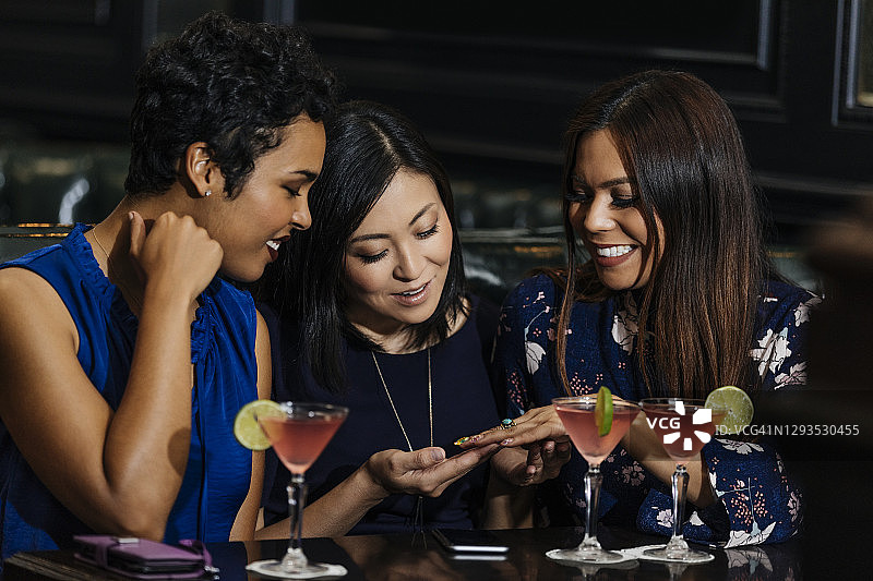 在酒吧和朋友喝酒时展示戒指的微笑女性图片素材