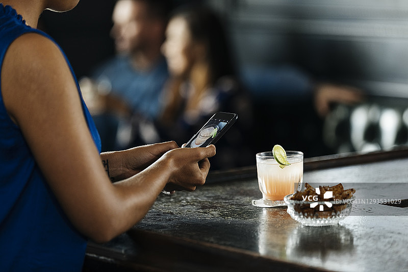女子在酒吧柜台用手机拍照的腰部特写图片素材