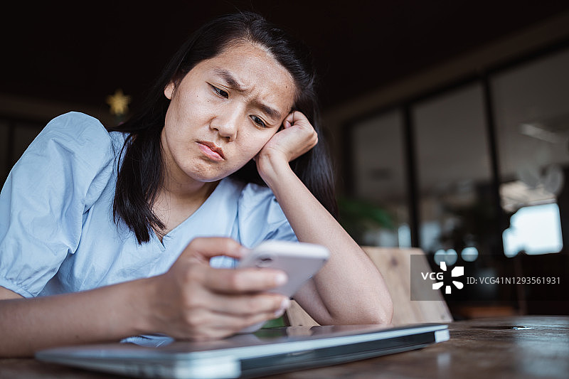 表情担忧地看着智能手机的年轻亚洲女性图片素材