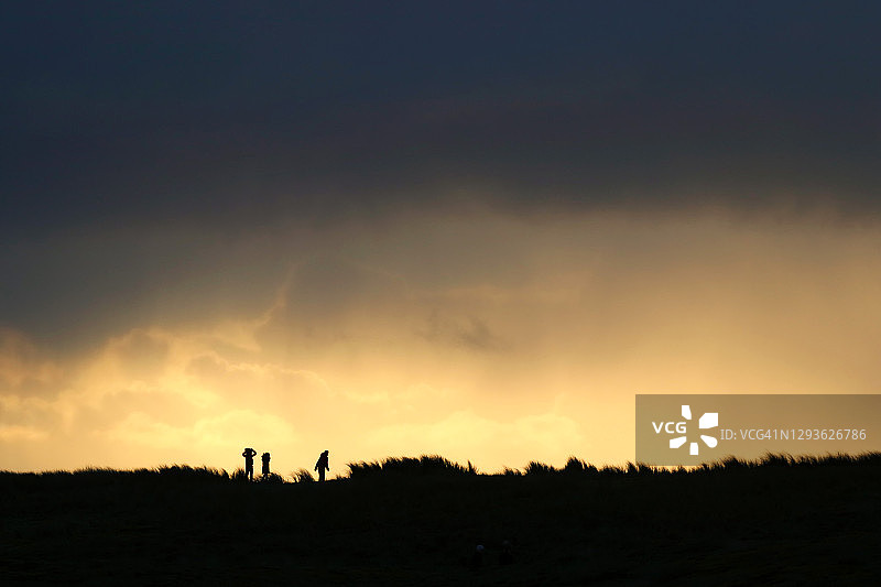 在法国诺曼底，一家人在日落时分在沙丘上行走的壮观景色图片素材