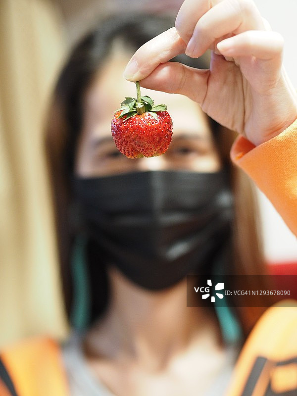 戴黑色口罩的女人在市场上手拿草莓吃街头小吃图片素材
