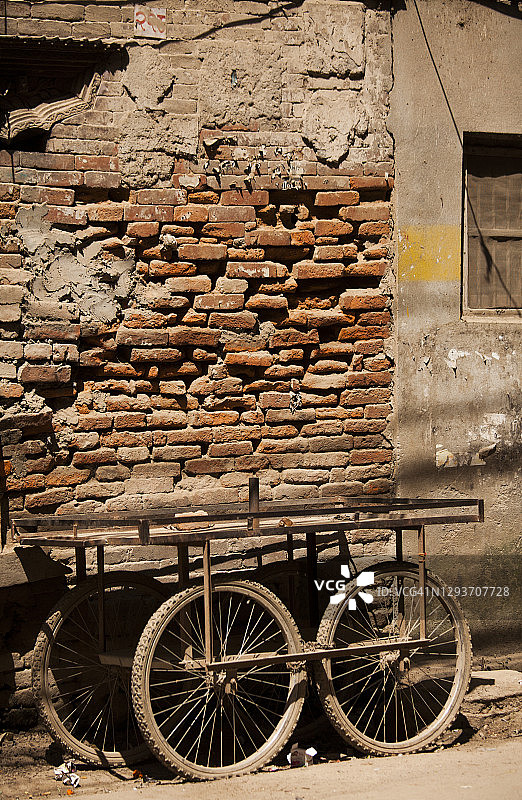 一辆摇摇晃晃的手推车停在路边，在尼泊尔加德满都的泰美尔，一幢废弃的砖砌建筑前。图片素材