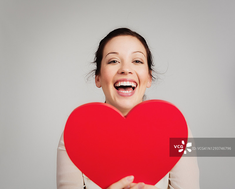恋爱中的年轻漂亮女人拿着一个巨大的红色爱心，庆祝情人节图片素材