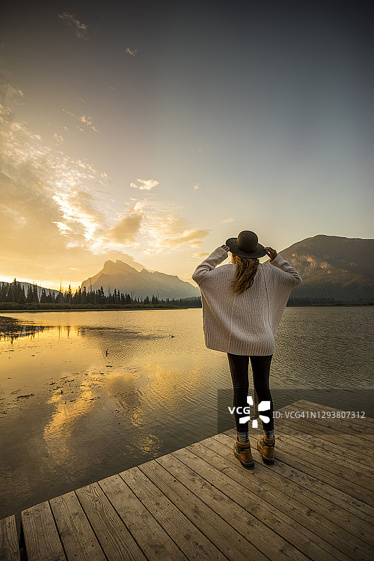 一位女士站在码头上，欣赏朱砂湖上的日出美景。图片素材