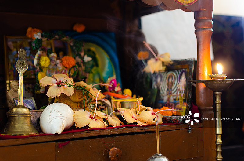 家中小型印度教寺庙的木制托盘侧视图，展示了由许多芙蓉花、油灯、香、海螺壳装饰的不同印度教神灵/女神偶像图片素材