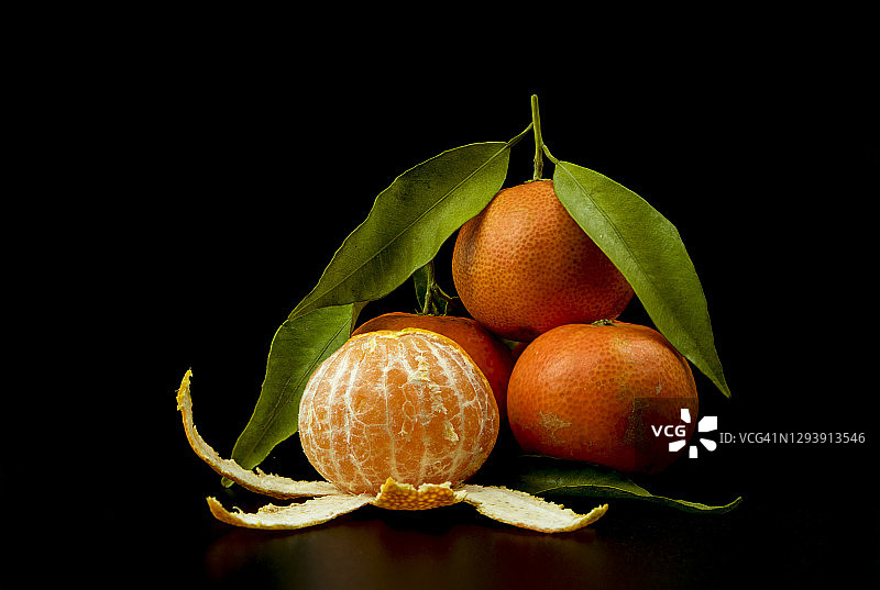 黑色背景上的新鲜成熟的橘子、果块和绿叶图片素材