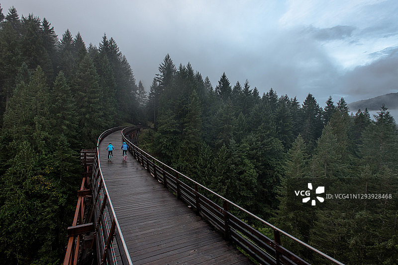 雨中老旧栈桥上骑自行车的年长女性航拍图片素材