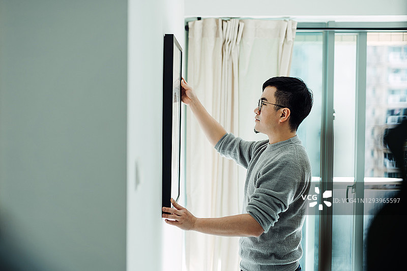 年轻亚洲男人手持画框装饰公寓图片素材
