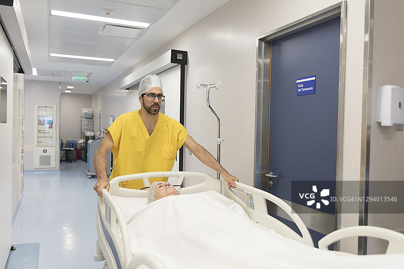 男护士沿医院走廊推动载有病人的医院病床图片素材