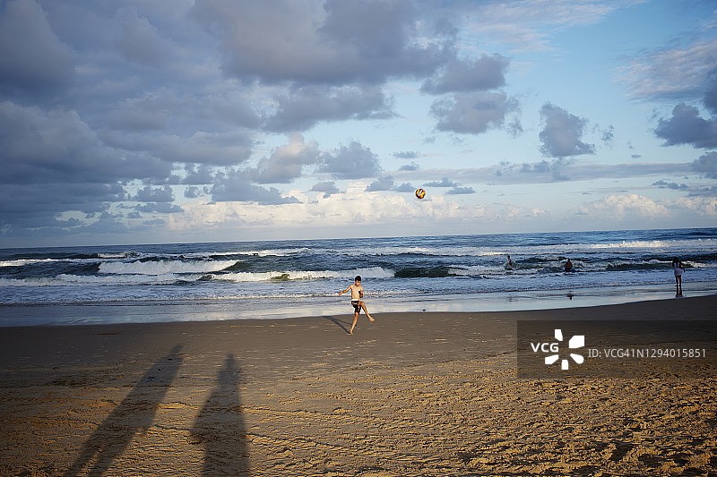 日落时男孩在海滩上踢球图片素材