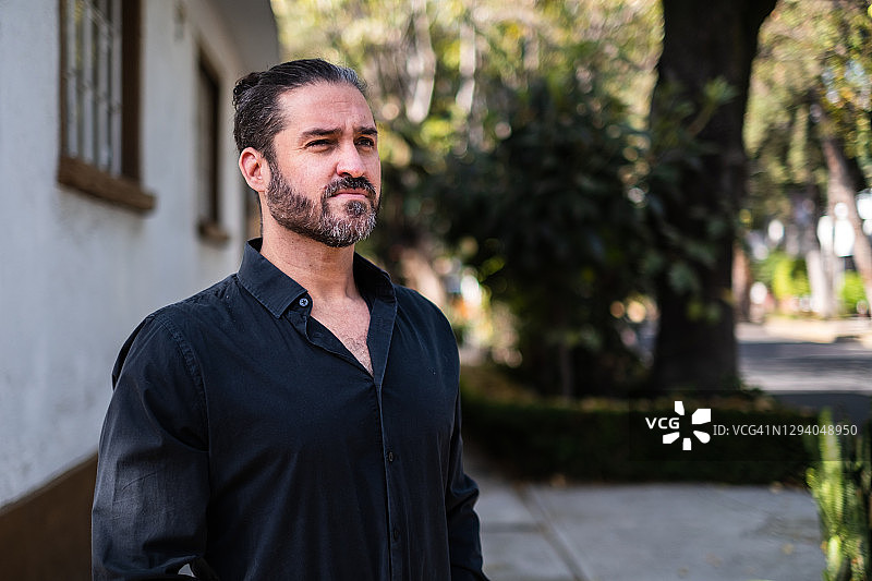 在城市街道上，穿着黑色衬衫看向远方的男人图片素材