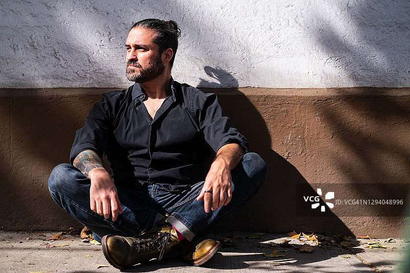 身穿黑衬衫，在城市街道人行道上盘腿而坐的男人图片素材