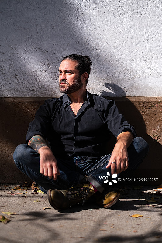 身穿黑衬衫，在城市街道人行道上盘腿而坐的男人图片素材