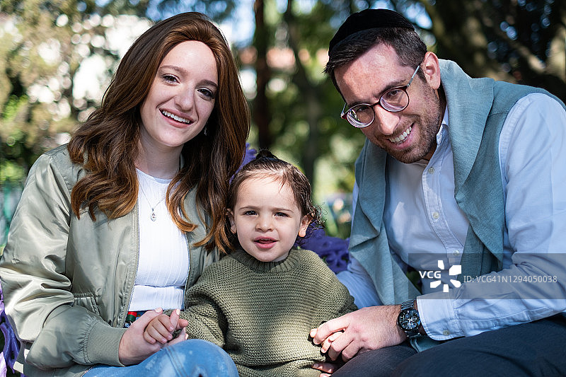 年轻的犹太家庭坐在公园长椅上，面对镜头图片素材