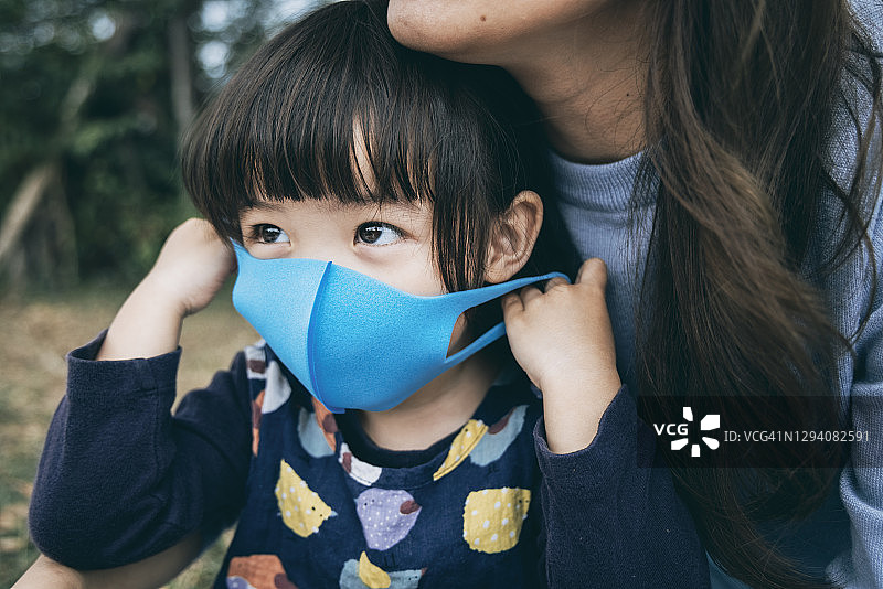 在公园里，母亲为小女儿戴上口罩，预防感冒、流感和病毒传播图片素材