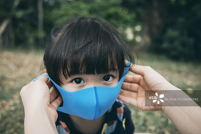 在公园里，母亲为小女儿戴上口罩，预防感冒、流感和病毒传播图片素材
