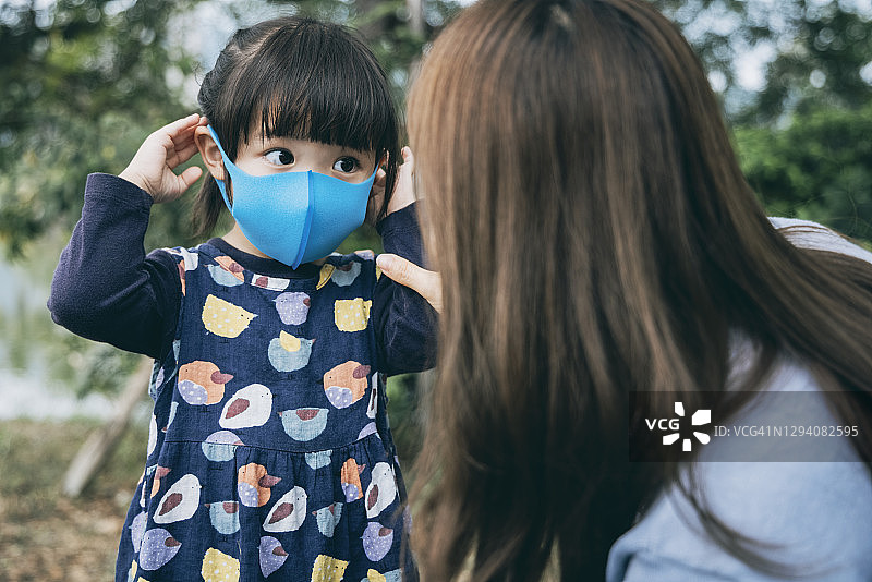 在公园里，母亲为小女儿戴上口罩，预防感冒、流感和病毒传播图片素材