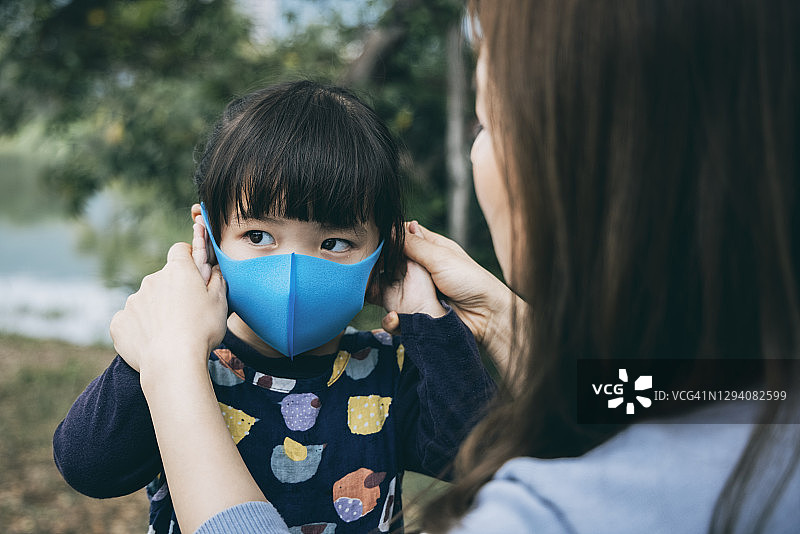 在公园里，母亲为小女儿戴上口罩，预防感冒、流感和病毒传播图片素材