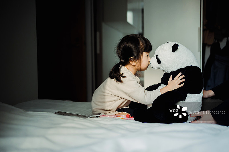 可爱的小亚裔女孩在家里的床上拥抱并亲吻她心爱的熊猫玩具图片素材