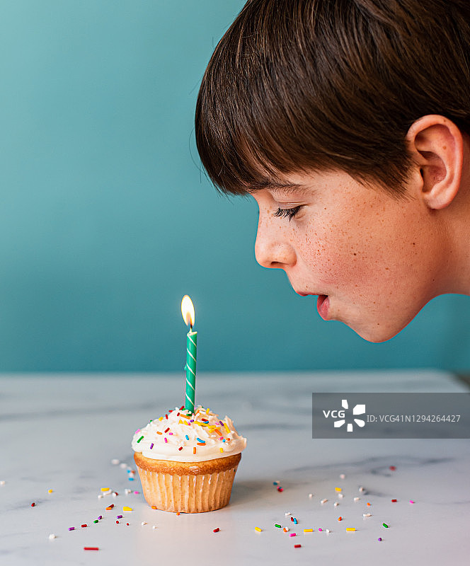 男孩吹灭纸杯蛋糕上的蜡烛，蛋糕上有糖霜和糖屑。图片素材