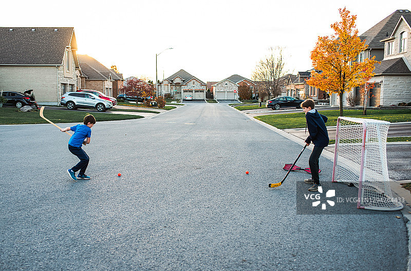 两个男孩在秋季住宅街道上打街头曲棍球图片素材