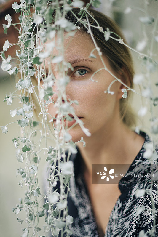 在绿色树叶植物后方，拥有蓝色眼睛的美丽女子肖像图片素材