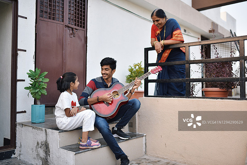 少年弹吉他，奶奶和妹妹在听音乐图片素材