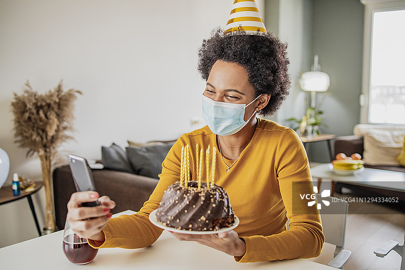 戴着口罩，通过手机视频通话庆祝生日的非洲裔妇女图片素材