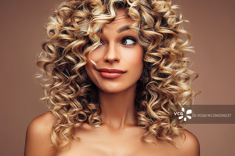 有着蓬松卷发的迷人年轻女人的棚拍肖像图片素材