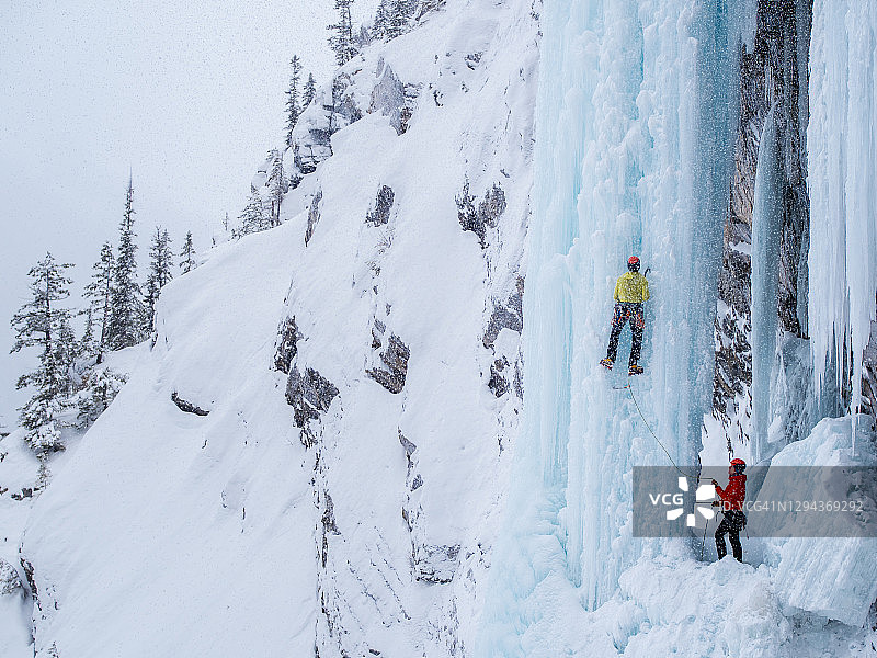 一名男子在攀登陡峭的冰柱时，手持冰镐，雪花飞舞图片素材