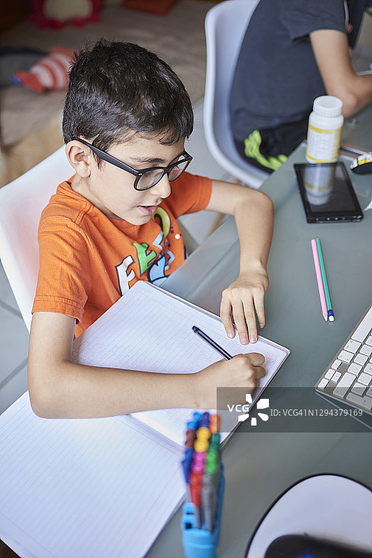 疫情封锁期间，两个（8-9岁，14-15岁）的男孩在家里的书桌上学习图片素材