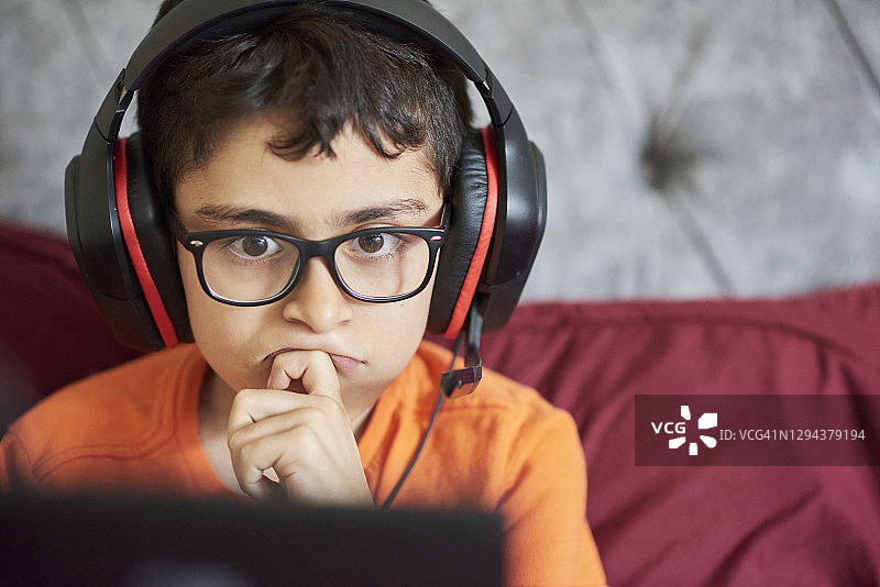 周末坐在床上用平板电脑玩游戏的男孩（8-9岁）图片素材