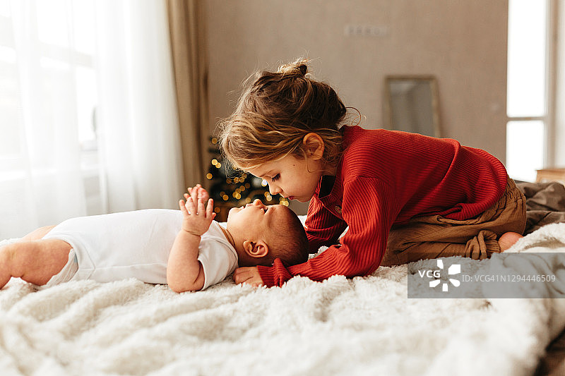 可爱孩子亲吻躺在白色床上的小妹妹图片素材