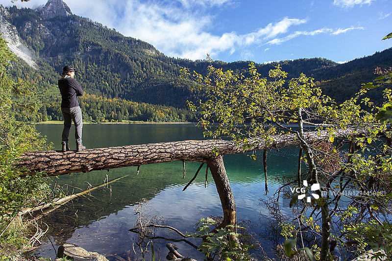 站在德国阿尔卑斯湖倒下的树上的白人男子图片素材