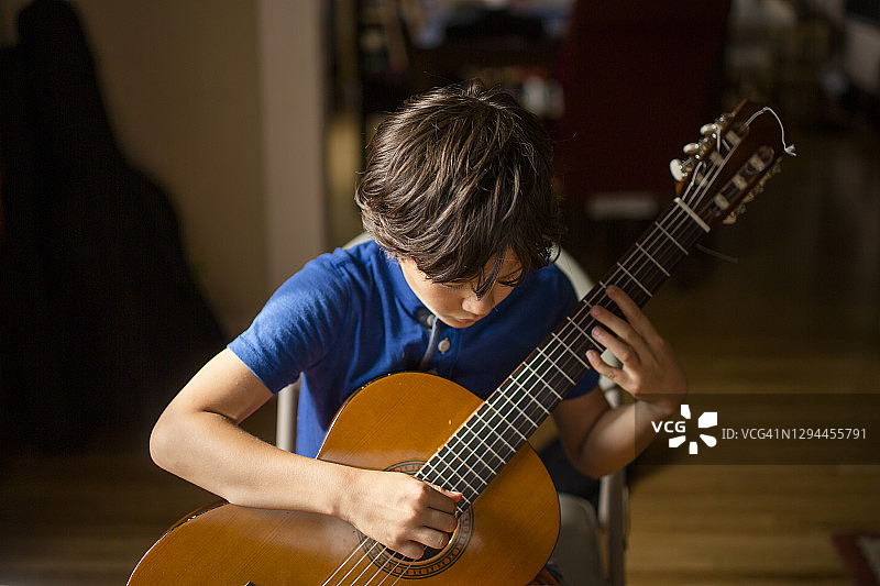 男孩在窗边光线下弯腰弹奏古典吉他图片素材