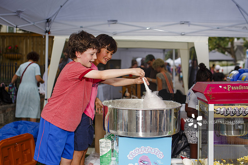 两个微笑的男孩在夏日街头集市一起制作棉花糖图片素材